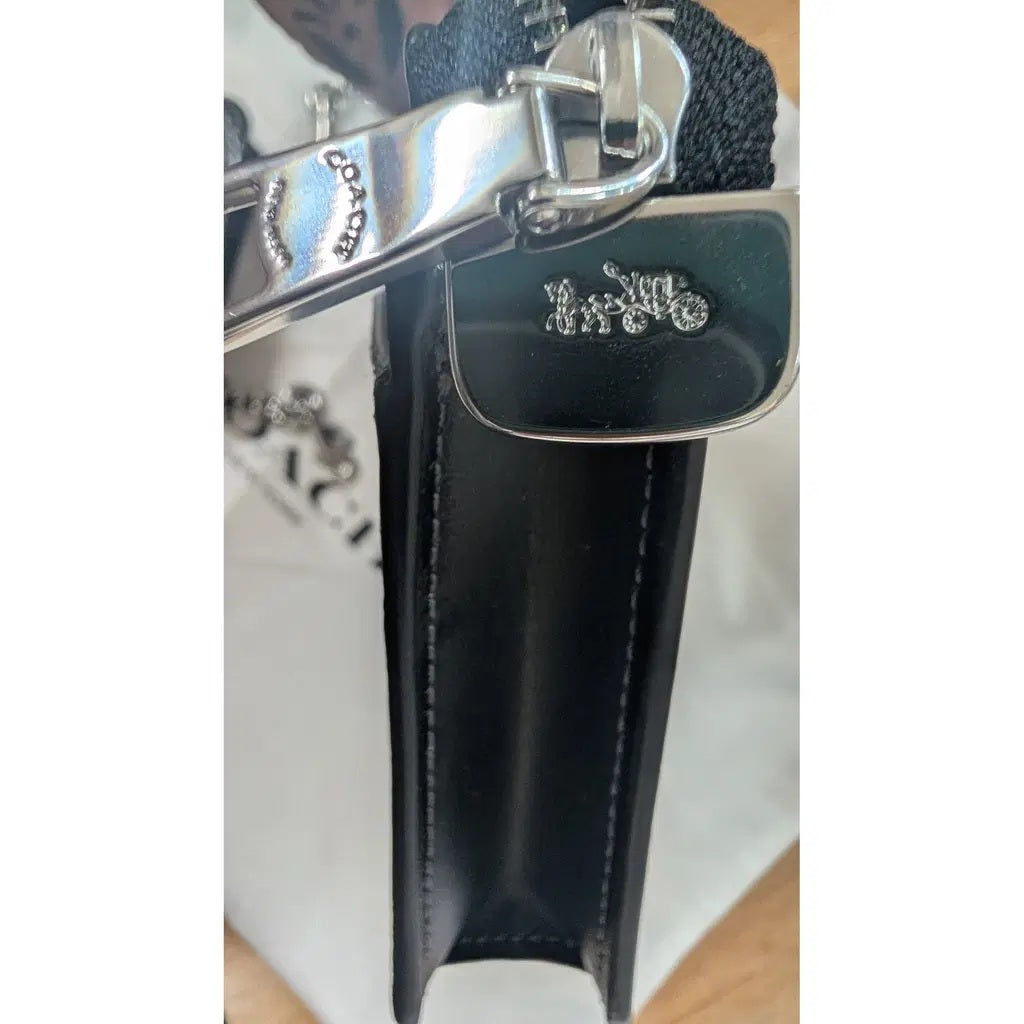 Close-up of a black leather Coach bag with a silver-tone metal carriage logo charm Pre-Owned Coach Black Celestial Print Crossbody Pouch Set – Excellent Condition