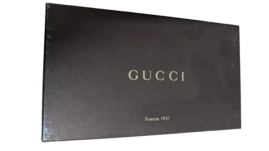 A dark brown Gucci box with gold lettering, placed on a light wood surface. Pre-Owned Gucci Interlocking G Wallet on Chain – Black Leather
