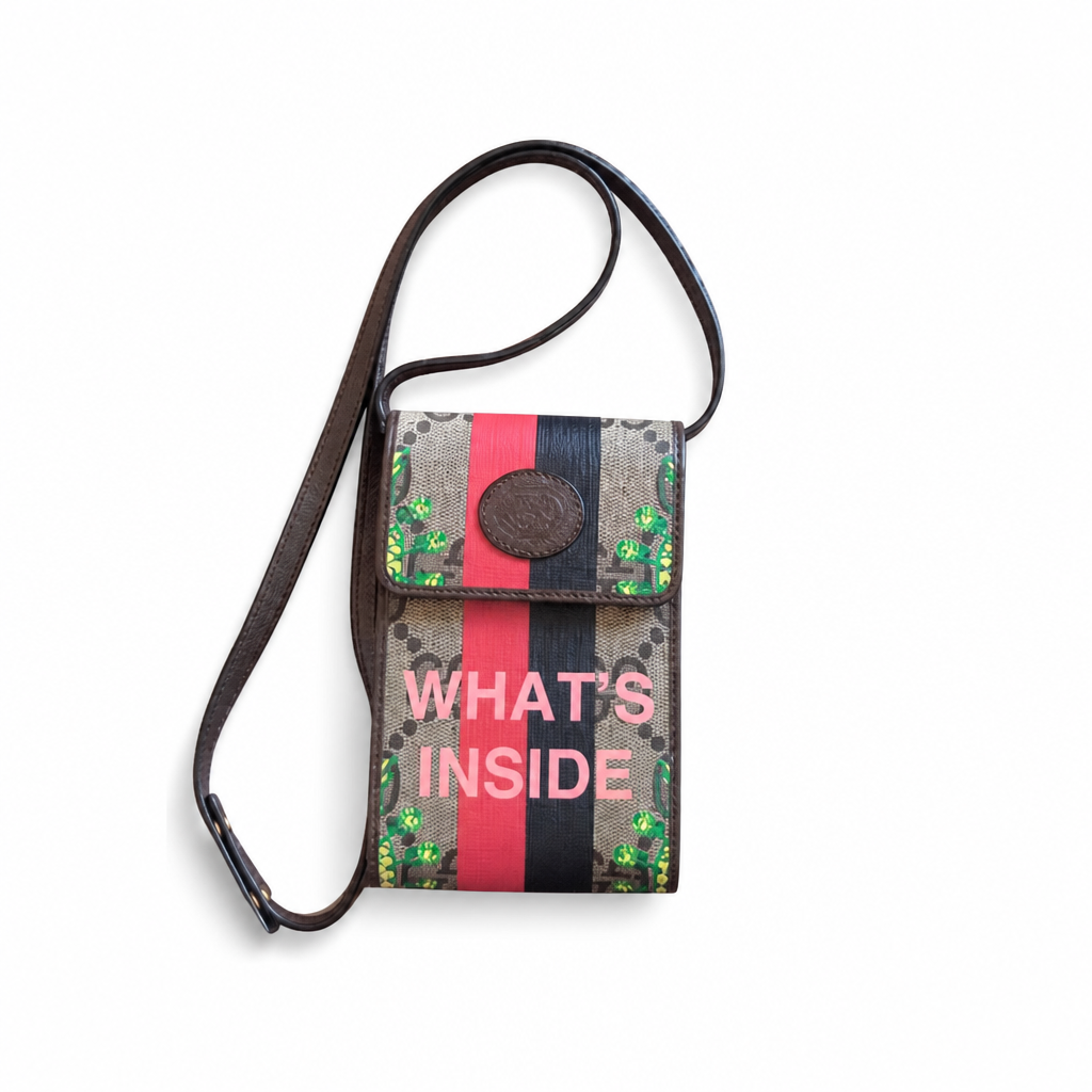 A Gucci-style canvas pouch with a brown leather strap, featuring the words 'WHAT'S INSIDE' in pink text over a red and black stripe design, on a white background. Pre-Owned Gucci x Ken Scott "What's Inside" Crossbody Phone Holder – GG Supreme Canvas – Full Set
