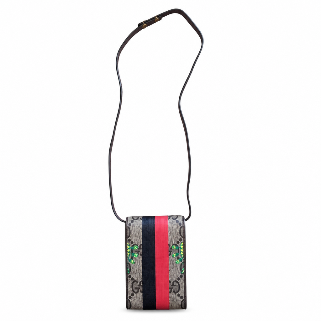 A Gucci crossbody bag with a black leather strap and a rectangular body featuring the classic GG Supreme monogram pattern, a central vertical stripe in navy, red, and beige, and green crystal embellishments. Pre-Owned Gucci x Ken Scott "What's Inside" Crossbody Phone Holder – GG Supreme Canvas – Full Set