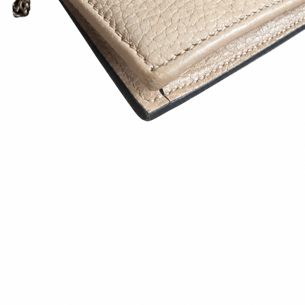 Close-up of a beige pebbled leather wallet corner with visible stitching and a dark edge, photographed on a plain white background.Pre-Owned Gucci Interlocking G Chain Wallet / Crossbody – Beige Pebbled Leather