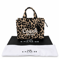 A Coach leopard print tote bag displayed on top of a black Coach dust bag with a white Coach dust bag in front, against a plain white background. Pre-Owned Coach Cargo Tote  Leopard Print Canvas Bag