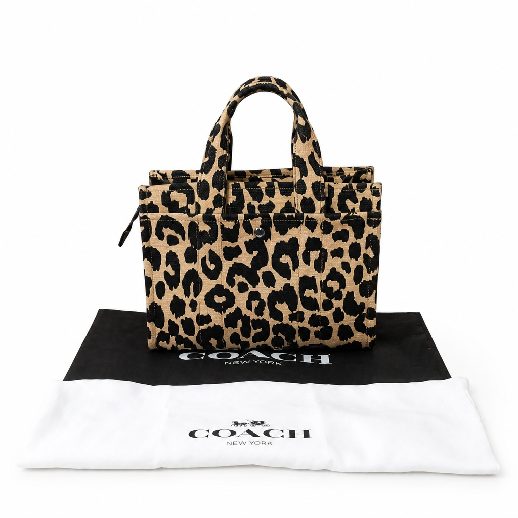 A Coach leopard print tote bag in beige and black, displayed on top of a black and white Coach dust bag against a white background. Pre-Owned Coach Cargo Tote  Leopard Print Canvas Bag