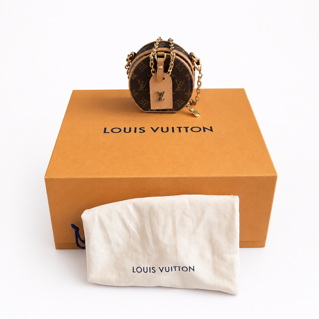 A Louis Vuitton monogrammed round shoulder bag with gold-tone chain straps, displayed on top of its signature orange box with a white dust bag in front. Pre-Owned Louis Vuitton Monogram Mini Boîte Chapeau Crossbody Bag – Full Set