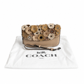 A Coach shoulder bag with a beige leather base and a top flap covered in 3D floral appliqués in tan, brown, and cream, displayed on top of its white Coach dust bag. Pre-Owned Coach Courier Wristlet with Floral Appliqué – Glovetanned Leather