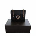 A black leather Gucci shoulder bag with a gold-tone chain strap and interlocking G logo, displayed on top of a black Gucci shoe box against a white background. Pre-Owned Gucci Interlocking Black shoulder bag 