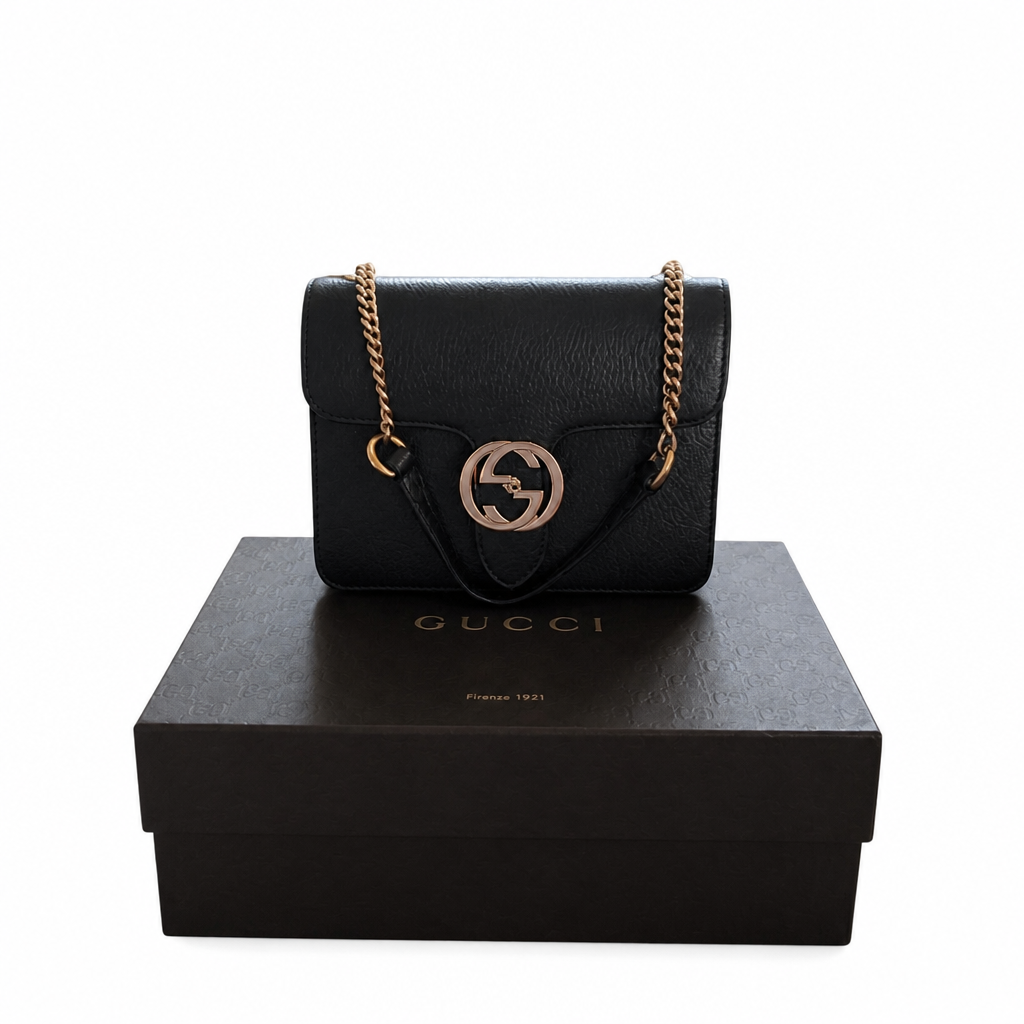 A black leather Gucci shoulder bag with a gold-tone chain strap and interlocking G logo, displayed on top of a black Gucci shoe box against a white background. Pre-Owned Gucci Interlocking Black shoulder bag 