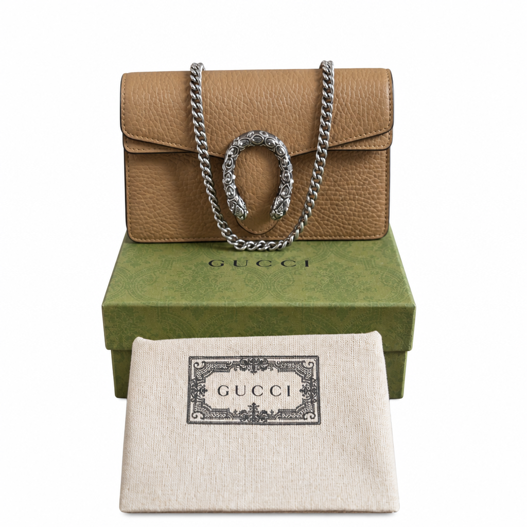 A Gucci shoulder bag in tan pebbled leather with a silver-tone chain strap and horsebit detail, displayed on top of a green Gucci box with a cream dust bag in front, all on a white background. Pre-Owned Gucci Dionysus Super Mini Crystal Tiger Head Chain Bag – Beige Leather