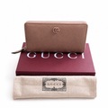 A tan leather zip-around wallet , displayed on top of a dark red Gucci box and a beige dust bag with a Gucci logo patch. Pre-Owned Gucci Interlocking G Zip-Around Continental Purse in Nude/Taupe Leather