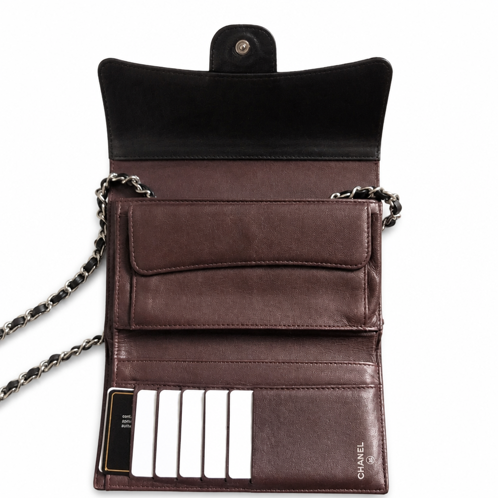 A dark brown leather wallet-style clutch with a black velvet interior flap, silver chain strap, card slots, and a visible Chanel logo on the lower right, shown open on a white background. Pre-Owned Chanel Classic Wallet on Chain WOC – Black Quilted Lambskin
