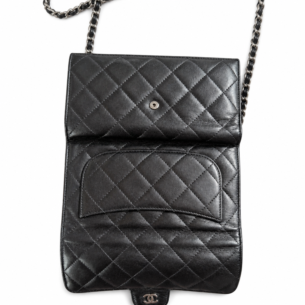 A black quilted leather shoulder bag with a silver chain strap and a small interlocking CC logo at the bottom, photographed against a plain white background. Pre-Owned Chanel Classic Wallet on Chain WOC – Black Quilted Lambskin
