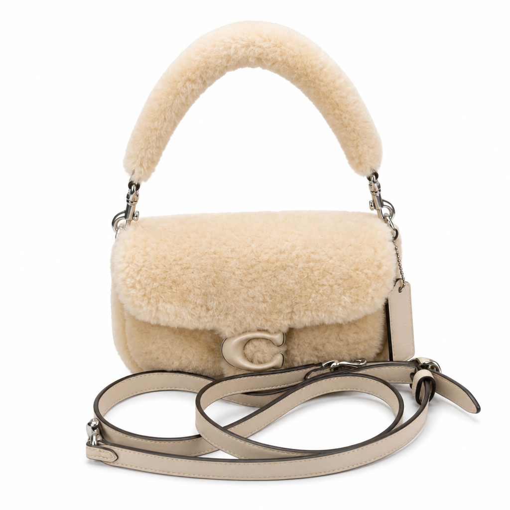 A beige sheepskin handbag with a curved top handle and a matching shoulder strap, featuring a silver-tone 'C' logo on the front. Pre-Owned Coach Tabby 18 Shearling Shoulder / Crossbody Bag – Cream