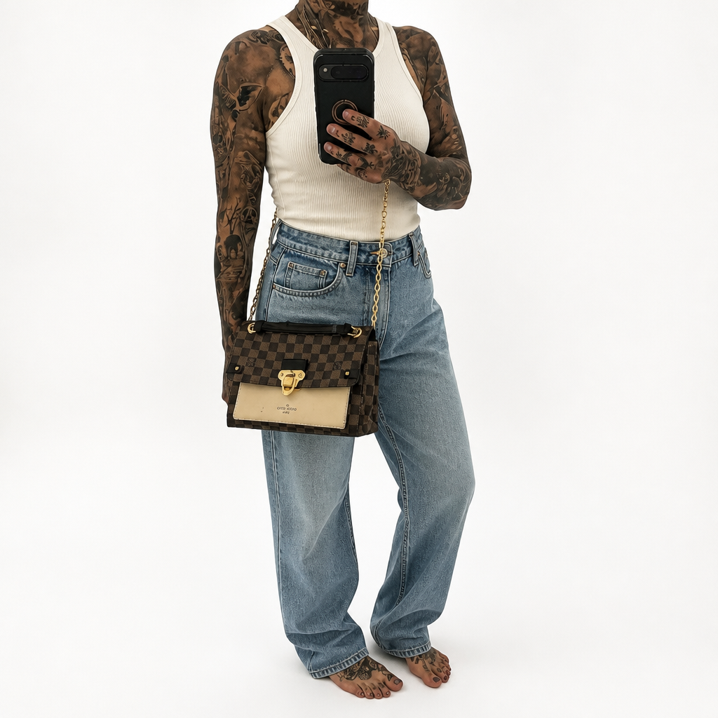 A person wearing a white tank top and light blue jeans holds a black phone while modeling a Louis Vuitton shoulder bag in the brand's signature brown checkerboard monogram canvas with a beige leather front panel and gold-tone hardware. Pre-Owned Louis Vuitton Vavin PM Damier Ebene / Crème – N40113