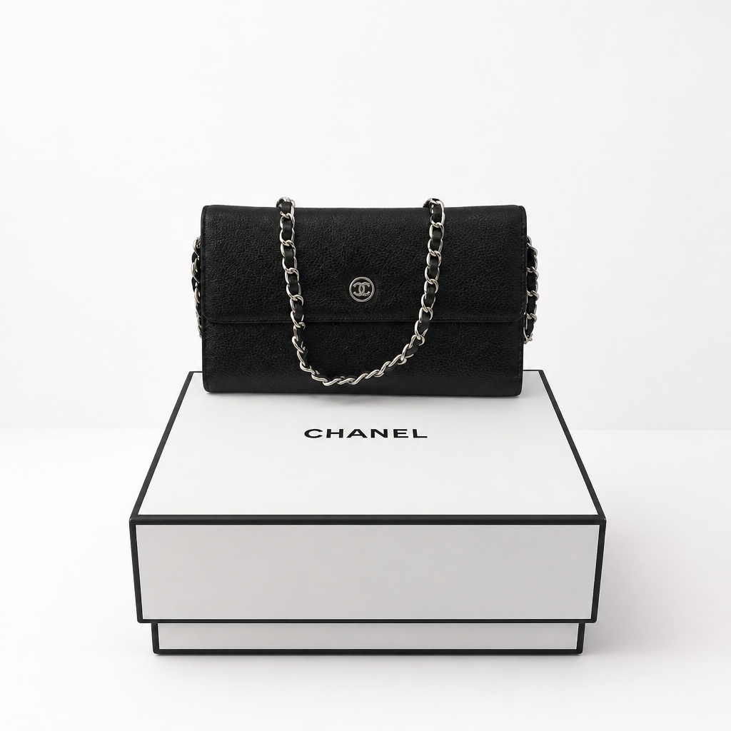 A black Chanel shoulder bag with a silver chain strap and interlocking CC logo, displayed on top of a white Chanel gift box against a clean white background. 