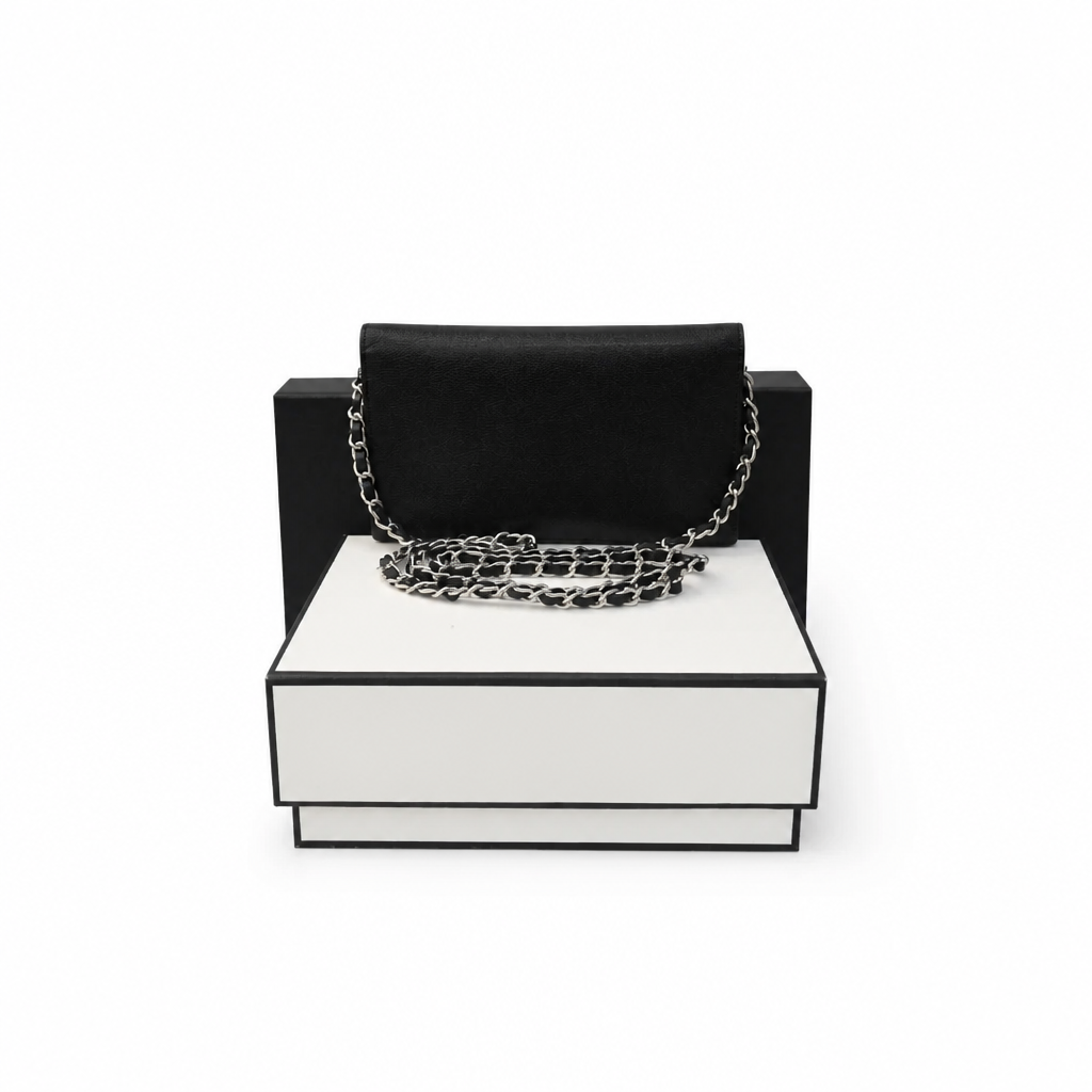 A black velvet clutch bag with a silver chain strap, displayed on a white and black presentation box against a white background. Pre-Owned Chanel Vintage Black Caviar Leather Wallet with Added Chain