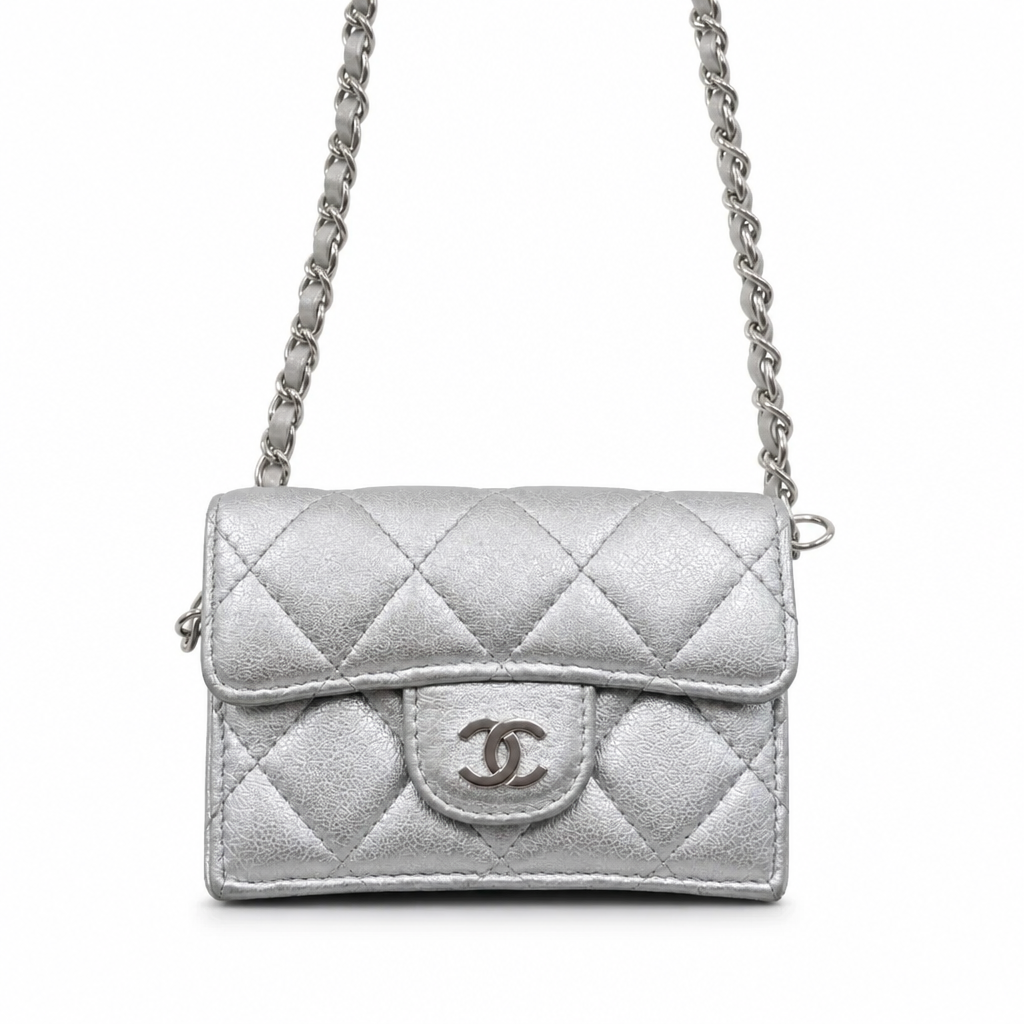 A silver quilted leather shoulder bag with a flap closure and a silver-tone interlocking CC logo on the front, shown against a plain white background. Pre-Owned Chanel Metallic Silver Matelassé Mini Chain Wallet / Micro Crossbody