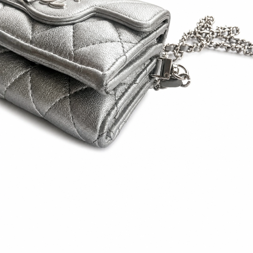 A close-up of a silver quilted leather clutch bag with a chain strap and silver-toned hardware, set against a plain white background. Pre-Owned Chanel Metallic Silver Matelassé Mini Chain Wallet / Micro Crossbody