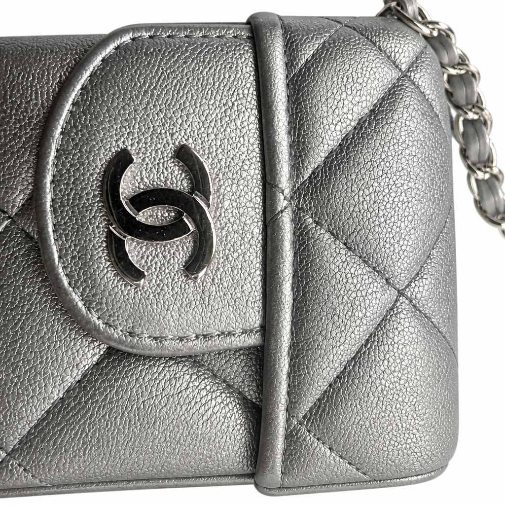 Close-up of a silver quilted leather handbag with a prominent interlocking CC logo on the front flap and a silver chain strap visible on the right side. Pre-Owned Chanel Metallic Silver Matelassé Mini Chain Wallet / Micro Crossbody