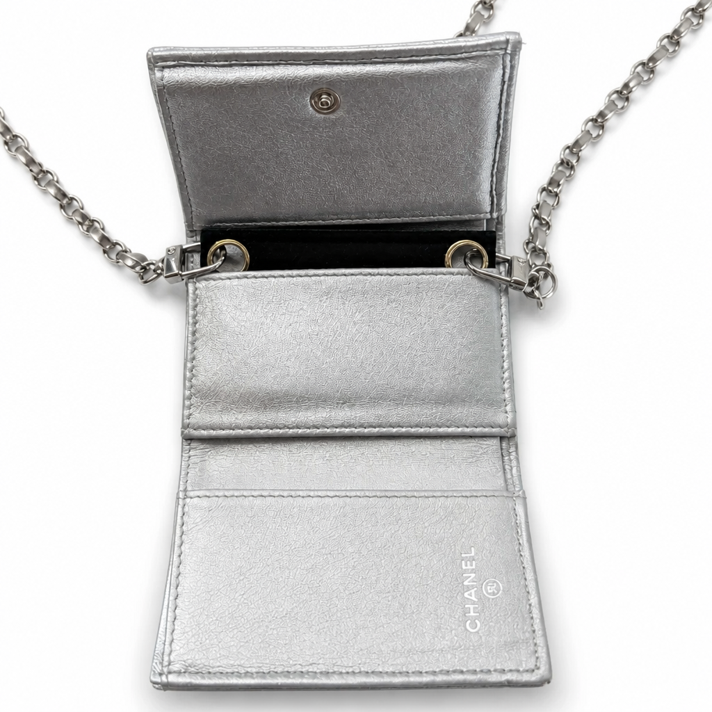 A silver metallic leather crossbody bag shown open, featuring a chain strap, card slots, and the CHANEL logo printed vertically on the lower right pocket. Pre-Owned Chanel Metallic Silver Matelassé Mini Chain Wallet / Micro Crossbody