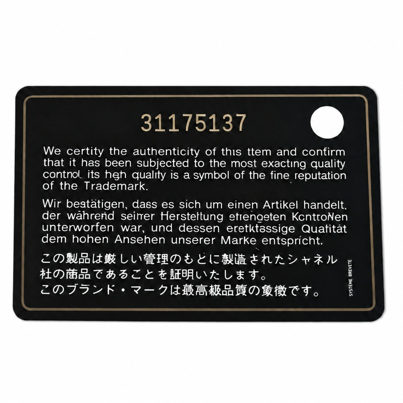 A black rectangular metal keychain plaque with gold lettering and Japanese text, featuring the number 31175137 in gold. A small silver keyring is partially visible at the top right on a white background. Pre-Owned Chanel Metallic Silver Matelassé Mini Chain Wallet / Micro Crossbody