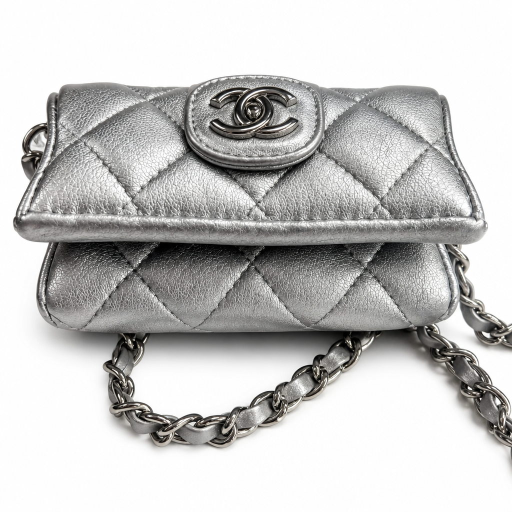 A silver quilted leather flap bag with a metal interlocking CC logo clasp and a silver chain strap, photographed on a white background. Pre-Owned Chanel Metallic Silver Matelassé Mini Chain Wallet / Micro Crossbody