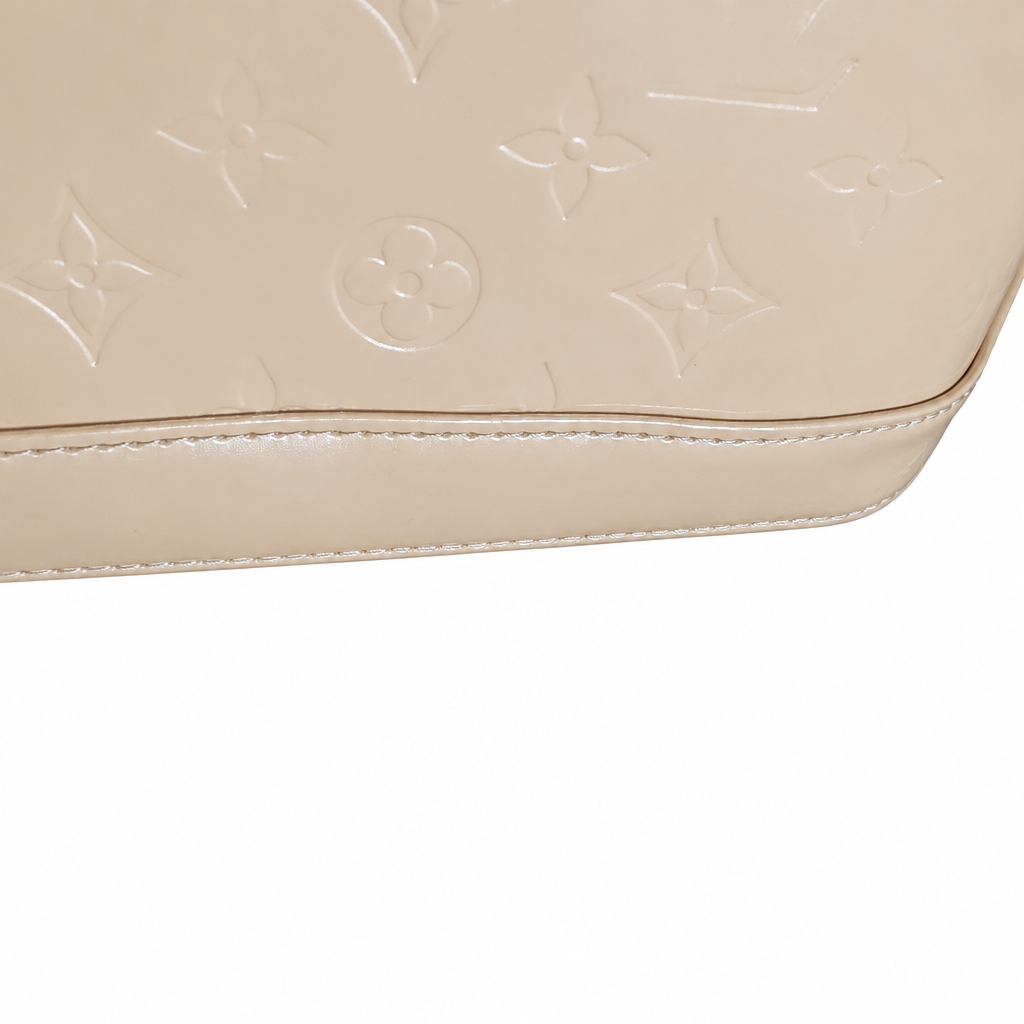 Close-up of a beige leather handbag with an embossed monogram pattern, showing the texture and stitching against a white background. Pre-Owned Louis Vuitton Alma PM Monogram Vernis – Beige Poudre