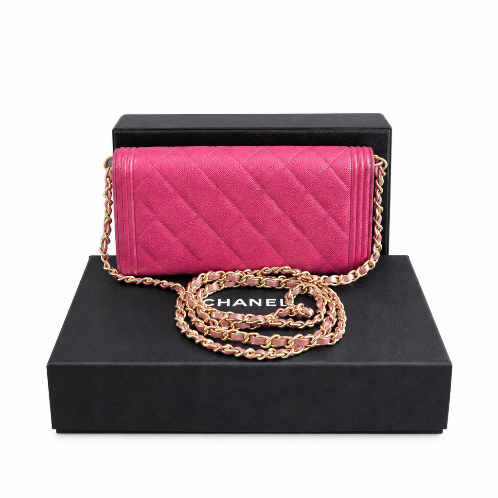 A Chanel quilted flap shoulder bag in vibrant pink suede, featuring a gold-tone chain strap, displayed on top of a black Chanel box. Pre-Owned Chanel Boy Wallet on Chain – Fuchsia Pink Caviar Leather – Gold Hardware