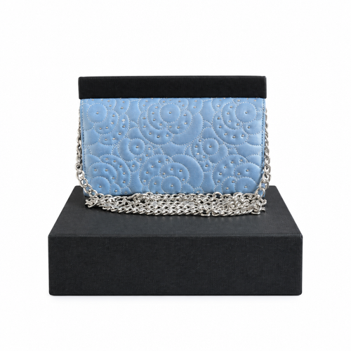 A light blue quilted evening clutch bag with silver chain strap, displayed on a black presentation box against a white background. Pre-Owned Chanel Camellia Studded Wallet on Chain WOC – Blue Lambskin