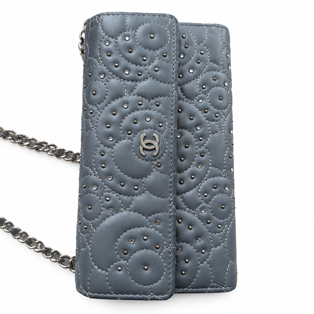 A Chanel shoulder bag in blue-gray leather with quilted circular stitching, studded details, and a silver-tone interlocking CC logo, shown on a white background with part of the chain visible. Pre-Owned Chanel Camellia Studded Wallet on Chain WOC – Blue Lambskin