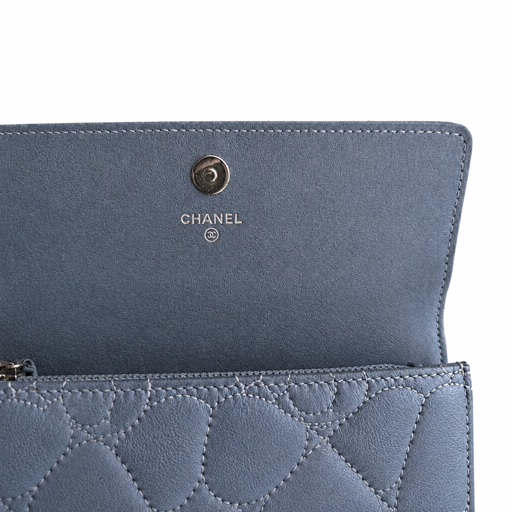 Close-up of a blue Chanel wallet or clutch showing the interior flap with a silver-tone metal snap button and the CHANEL logo, alongside the quilted exterior. Pre-Owned Chanel Camellia Studded Wallet on Chain WOC – Blue Lambskin
