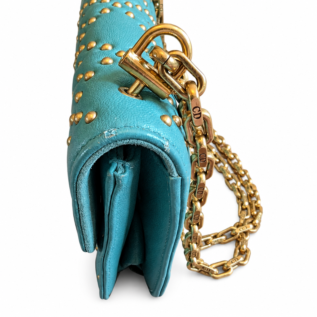 Close-up of a turquoise blue leather handbag with gold studs, a gold clasp, and a gold chain strap on a white background. Pre-Owned Christian Dior Small DiorAddict Cannage Studded Flap Bag – Light Blue Lambskin