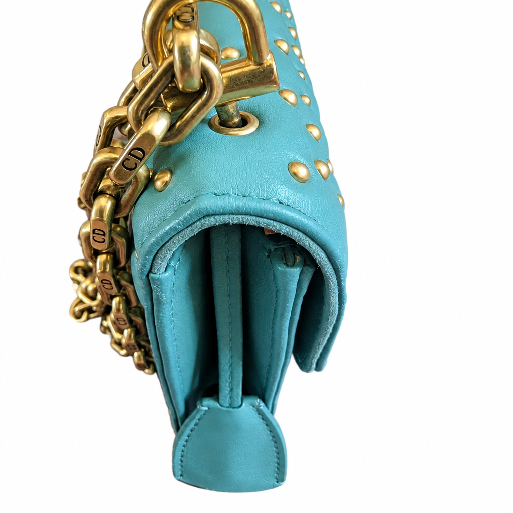A close-up of a turquoise blue leather handbag with gold hardware, featuring a chunky gold chain strap engraved with 'CD' and gold studs on the exterior. Pre-Owned Christian Dior Small DiorAddict Cannage Studded Flap Bag – Light Blue Lambskin