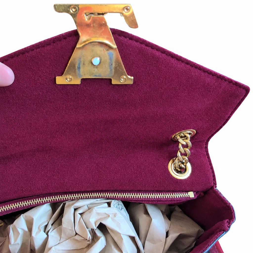Close-up of a burgundy suede handbag interior with gold-tone hardware, including a large decorative letter clasp and a chain detail, with crumpled tissue paper visible inside. Pre-Owned Louis Vuitton Passy Monogram Shoulder Bag – Burgundy Interior