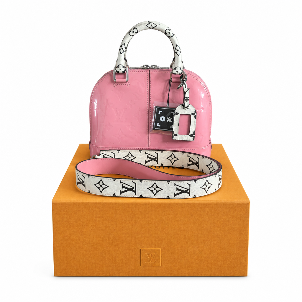 A pink patent leather Louis Vuitton handbag with a white monogram shoulder strap and matching charm, displayed on top of an orange Louis Vuitton box against a white background. Pre-Owned LOUIS VUITTON ALMA BB – ROSE BLUSH MONOGRAM VERNIS MIROIR