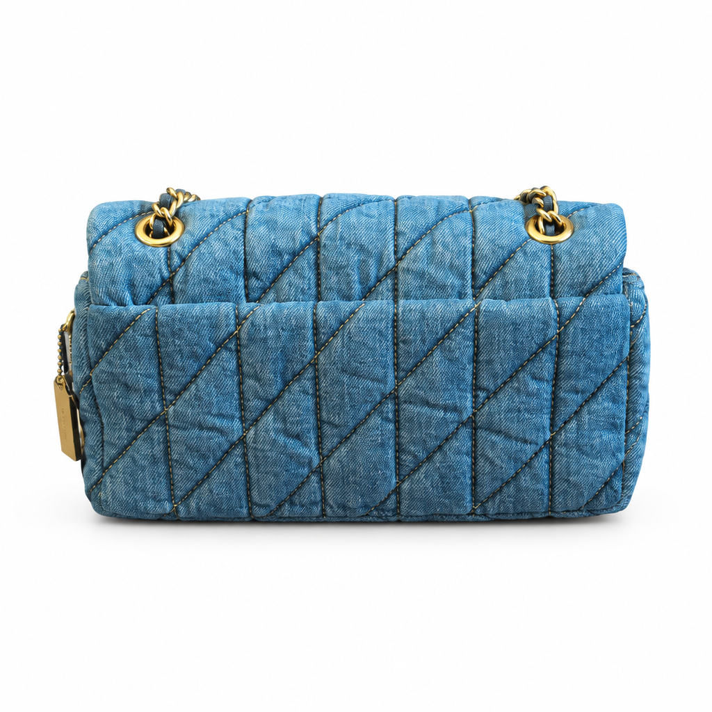 A blue quilted denim shoulder bag with a diagonal stitched pattern and gold-tone chain details, shown against a plain white background. Pre-Owned Coach Quilted Tabby Shoulder Bag 26 – Blue Denim