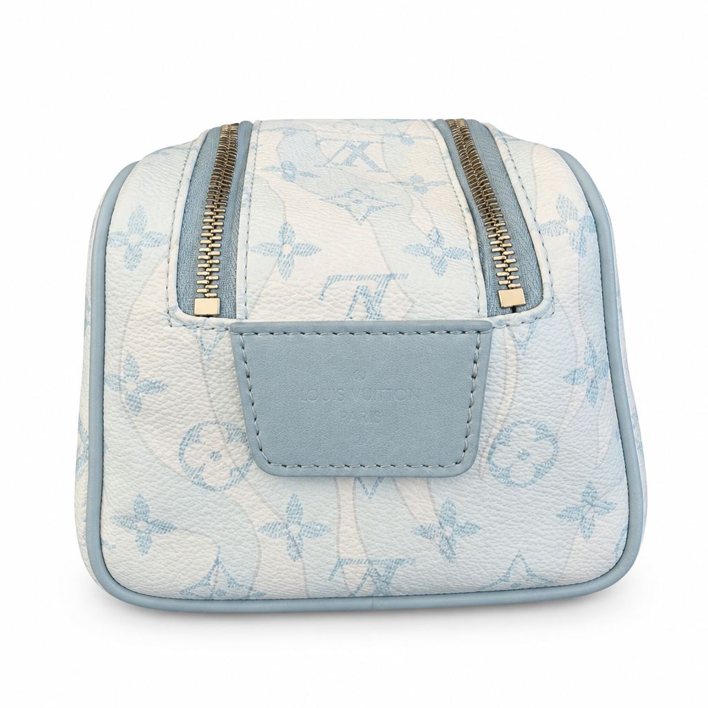 A small Louis Vuitton toiletry bag in light blue and white monogram canvas with gold-tone zippers and a stitched front patch, shown on a clean white background. Pre-Owned Louis Vuitton x Richard Prince Limited Edition Monogram Bag – Spring/Summer 2008 – Pale Blue