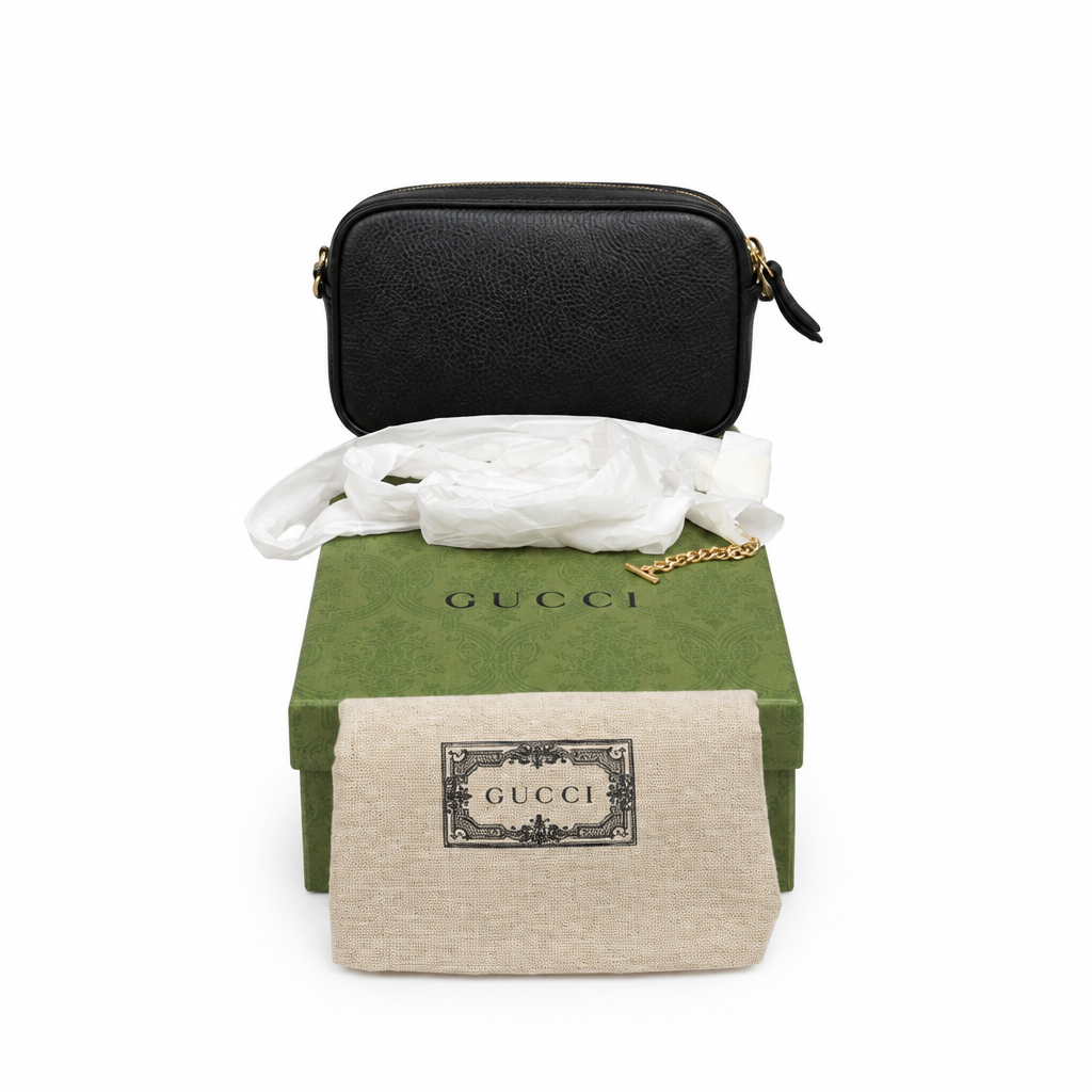 A black pebbled leather Gucci shoulder bag with gold-tone hardware, displayed above its green Gucci box, white tissue paper, and beige dust bag on a white background. Pre-Owned Gucci GG Marmont Black Leather Camera Crossbody Bag – Gold Hardware