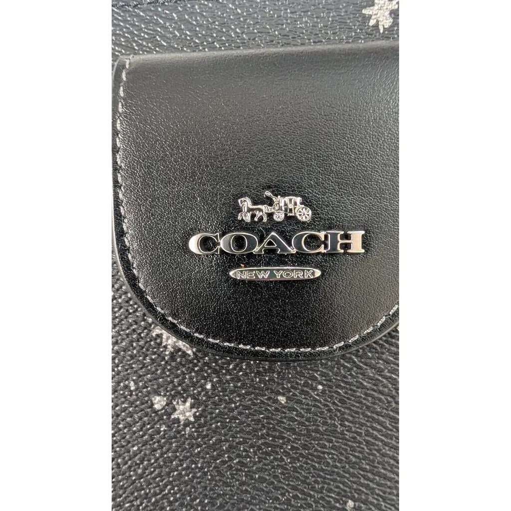 Close-up of a black Coach New York leather accessory featuring the silver-tone metallic Coach logo and horse-and-carriage emblem on a textured background. Pre-Owned Coach Black Celestial Print Crossbody Pouch Set – Excellent Condition