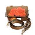 A brown leather shoulder bag featuring a large orange rose painting on the front flap, shown with its matching brown leather strap and gold-tone hardware on a white background. Pre-Owned Coach Tom Wesselmann Rogue Top Handle Bag
