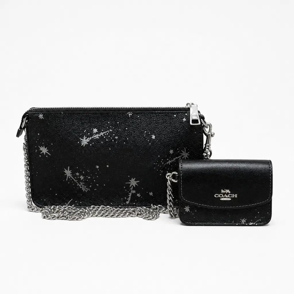 A Coach black leather crossbody clutch and matching wallet set, both decorated with silver star and shooting star prints, featuring silver chain straps and a silver-tone Coach logo on the front of the wallet. Pre-Owned Coach Black Celestial Print Crossbody Pouch Set – Excellent Condition