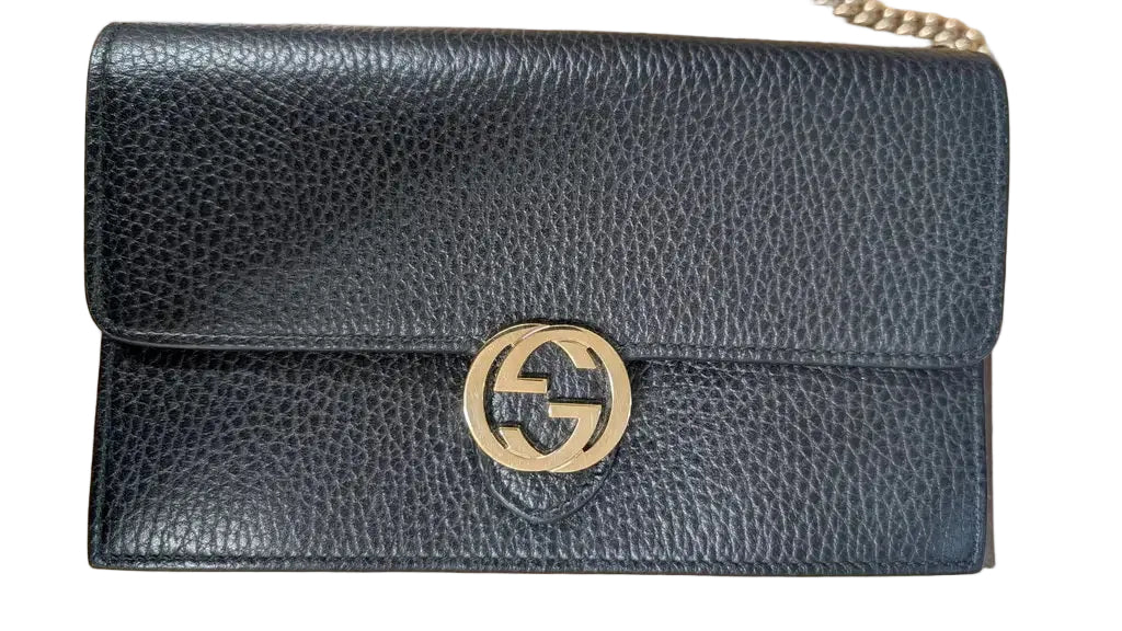 A black pebbled leather shoulder bag with a gold-tone interlocking G logo on the front, resting on a light wood surface. Pre-Owned Gucci Interlocking G Wallet on Chain – Black Leather