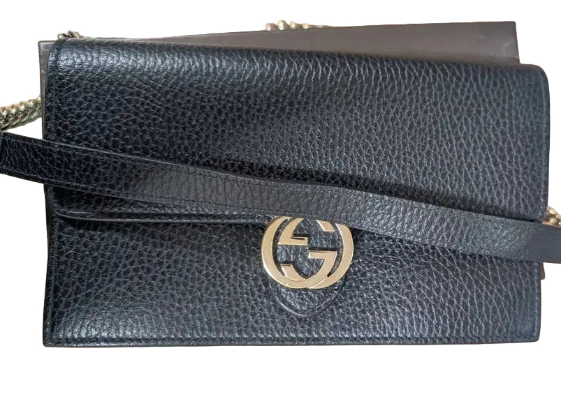 A black pebbled leather shoulder bag with a gold-tone interlocking G logo clasp, resting on a light wood surface. Pre-Owned Gucci Interlocking G Wallet on Chain – Black Leather