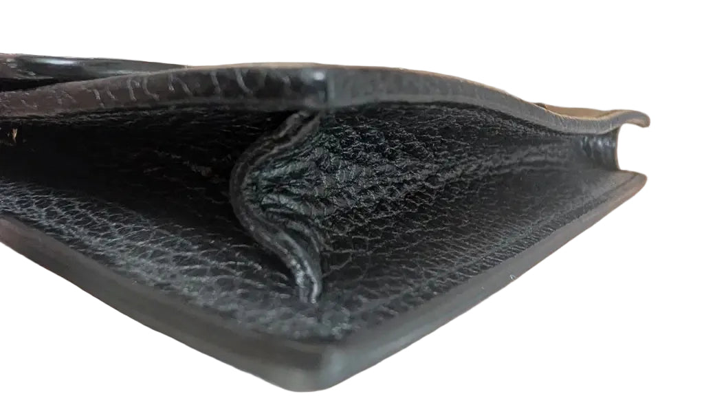 A close-up of a black textured leather wallet or clutch being held open by a hand, showing the interior lining and a gold-tone chain strap on a wooden surface. Pre-Owned Gucci Interlocking G Wallet on Chain – Black Leather