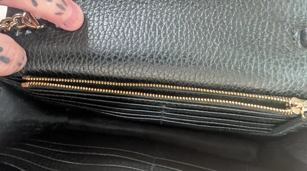 Close-up of a black pebbled leather clutch or wallet showing a gold-tone zipper and interior card slots, with a hand holding the edge. Pre-Owned Gucci Interlocking G Wallet on Chain – Black Leather