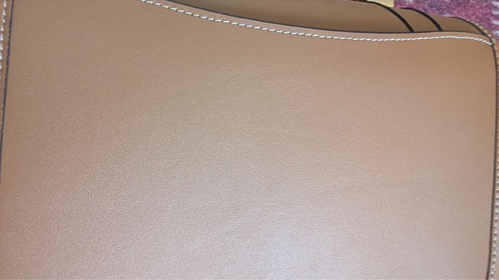 Close-up of a tan leather or faux-leather surface with visible grain texture and white contrast stitching along the curved edge. Pre-Owned Coach Tom Wesselmann Rogue Top Handle Bag