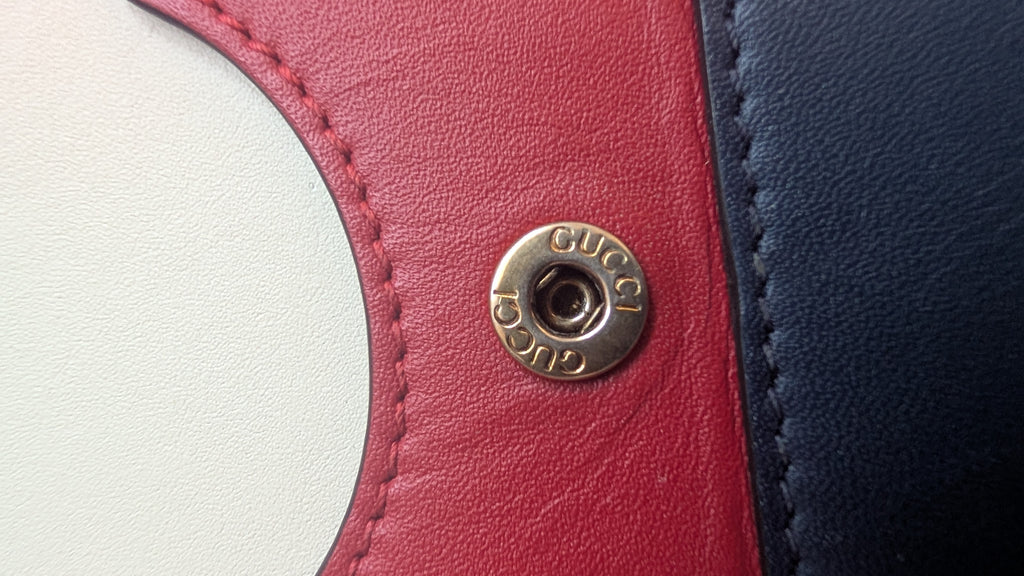 Close-up of a Gucci logo on a red and blue leather product.