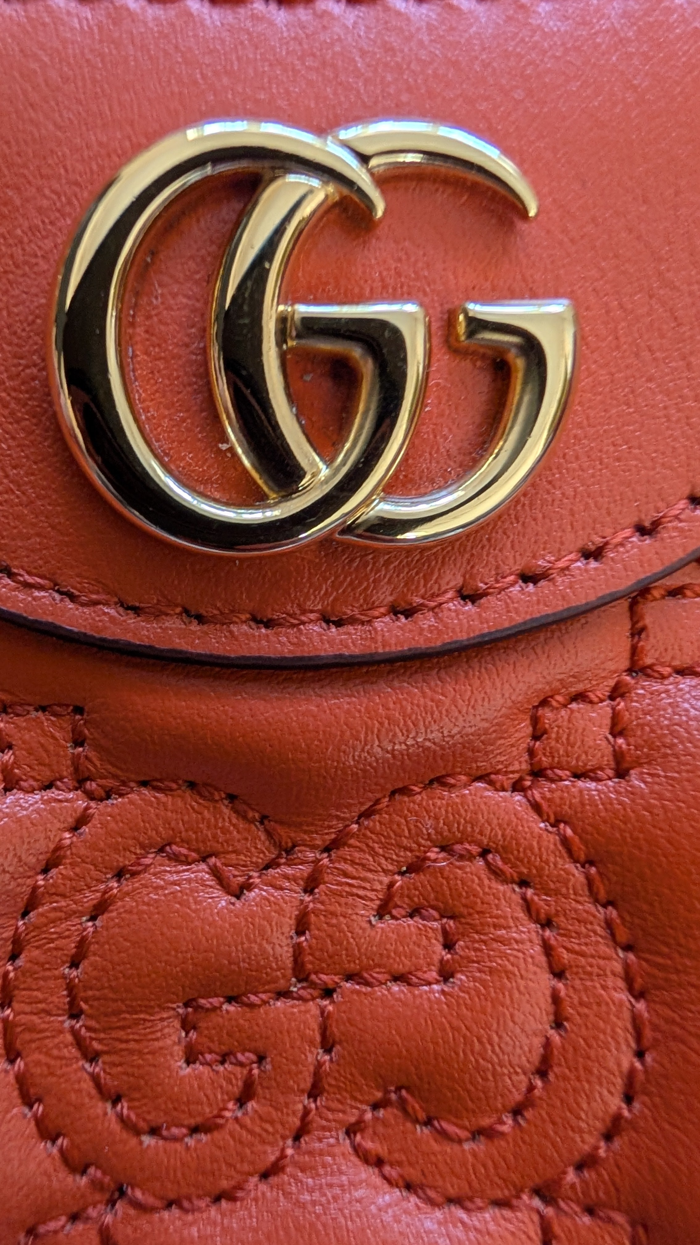 Close-up of a orange Gucci handbag with gold logo.Pre-owned Gucci GG Quilted Matelasse Leather Mini Shoulder Bag In Orange