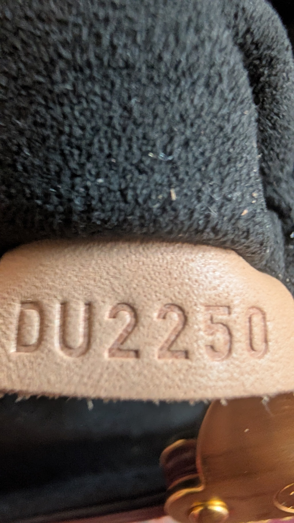 Close-up of a dark charcoal fleece or sherpa fabric item with a beige leather or faux-leather trim embossed with the text 'DU2250'. Pre-Owned Louis Vuitton Duffle Bucket Monogram Canvas - Full Set