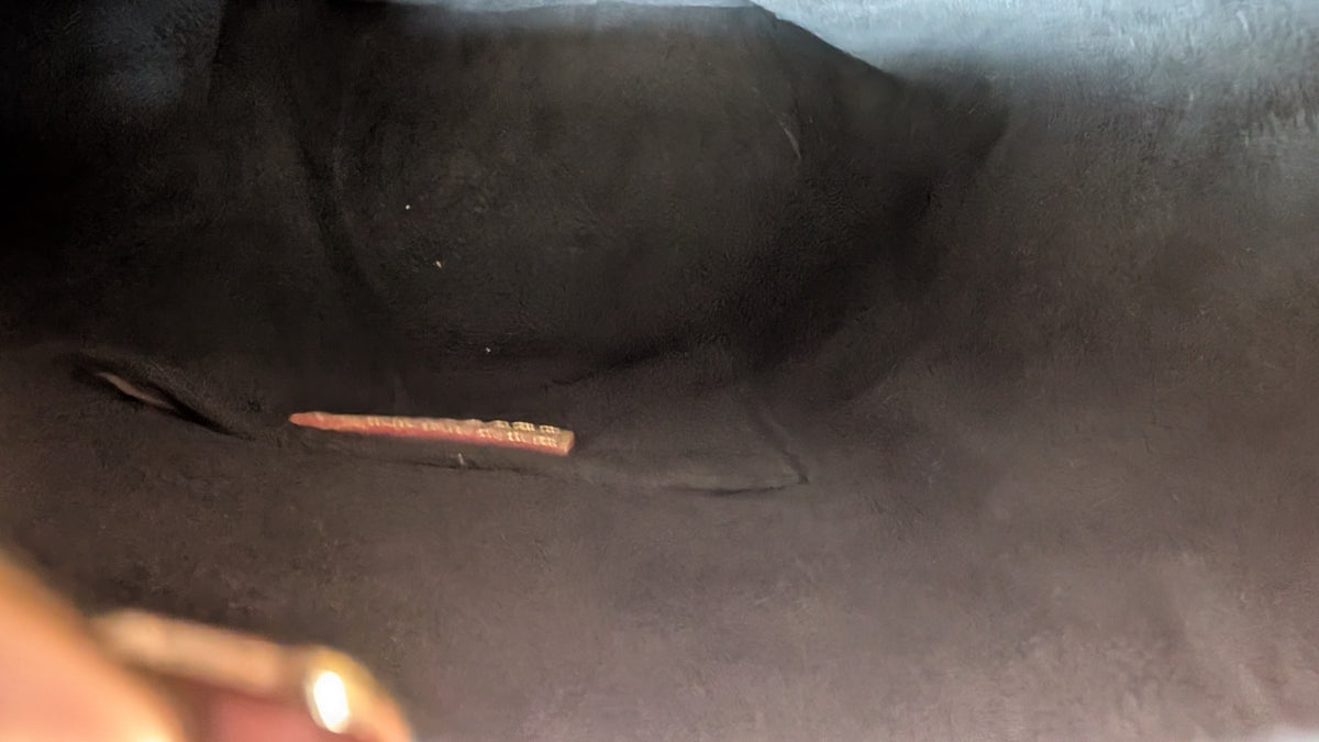 Close-up of a dark textured fabric interior with a small metallic reddish-brown bar or piece resting inside a pocket or crevice. Pre-Owned Louis Vuitton Duffle Bucket Monogram Canvas - Full Set