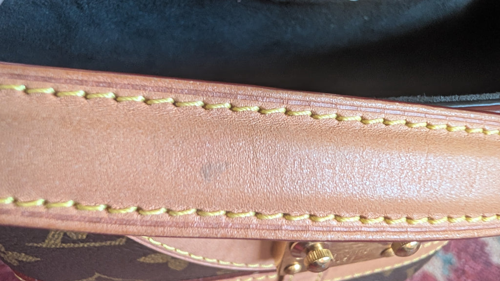Close-up of a tan leather strap with gold-colored stitching and a small gold metal clasp, set against a dark background. Pre-Owned Louis Vuitton Duffle Bucket Monogram Canvas - Full Set
